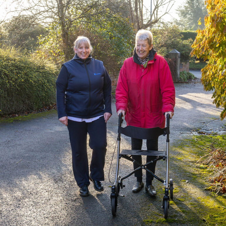 Houlbrook Physiotherapy specialist supporting an elderly patient during a mobile rehabilitation session using a walking frame in a bright, outdoor setting.