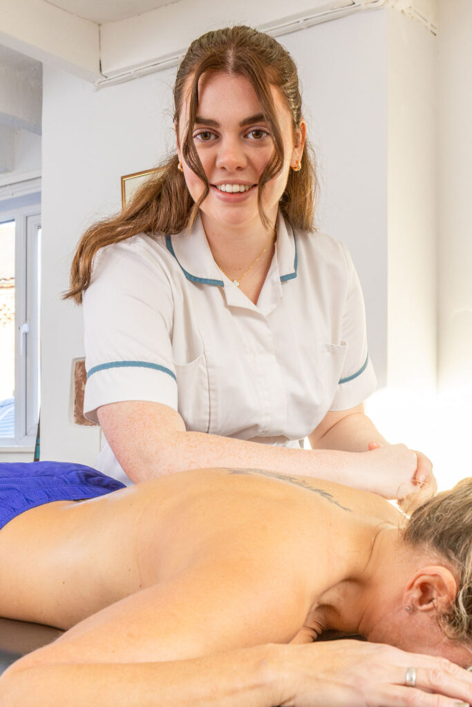 Therapist uses her elbow to apply deep tissue massage to patients back whilst they lie on a plinth
