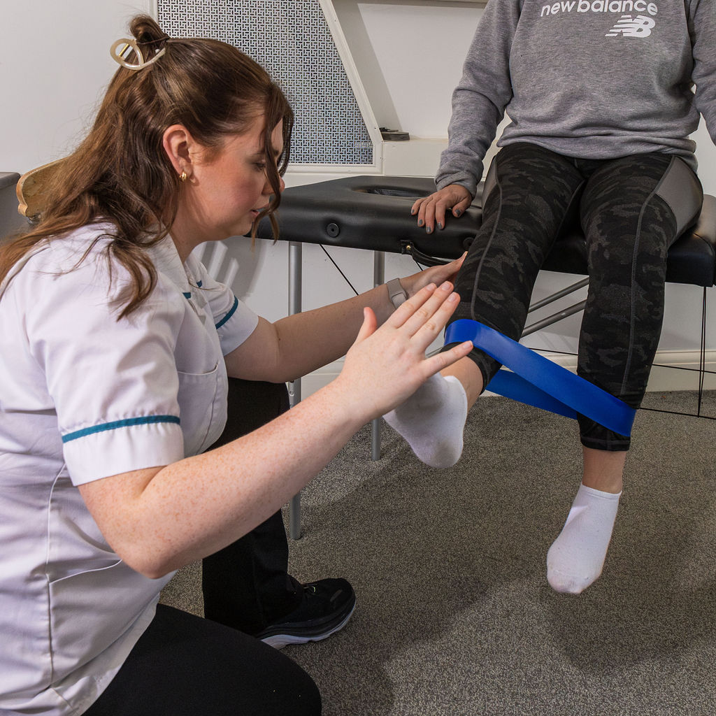 Physio assitant uses theraband with a patient to build strength in the quads.