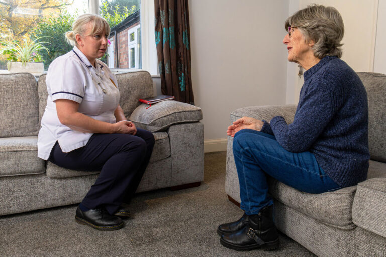 physiotherapist and patient sit opposite one another on grey sofa's talking.